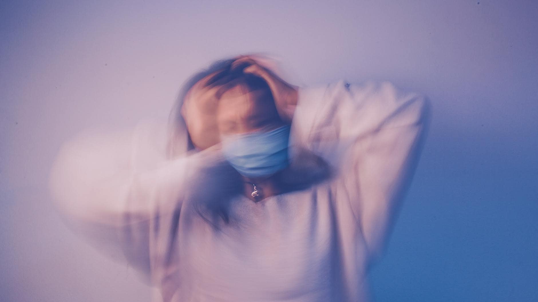 woman in face mask touching head in anxiety