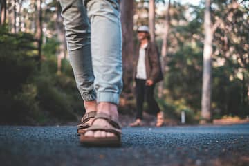crop unrecognizable person in sandals walking on asphalt sidewalk