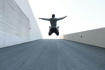 man in gray hoodie jump with open arms