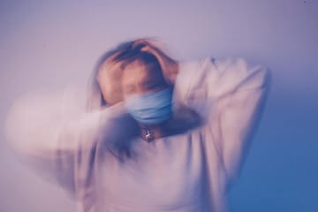 woman in face mask touching head in anxiety